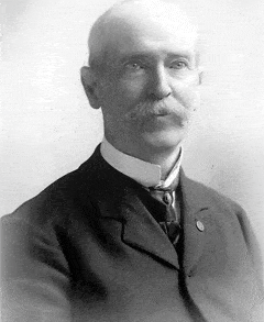 Charles E Meyer Charles E. Meyer; Past Supreme MAGI; Black and white portrait of an older man with a bald head and a bushy mustache, wearing a dark suit with a high-collared shirt and a tie, facing slightly to the viewer’s left.