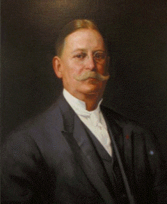 Thomas J. Shryock Thomas J. Shryock; Past Supreme MAGI; Portrait of a middle-aged man with a large mustache, wearing a dark suit, white shirt, and vest. He has short, neatly combed hair and is posed against a dark background, looking directly ahead.
