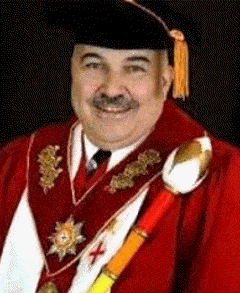 William H. Koon William H. Koon II, 2007 to 2019 Past Supreme MAGI; A man wearing ceremonial academic regalia, including a red and gold robe, ornate decorations, a sash, and a black cap with a gold tassel, smiles against a dark background.